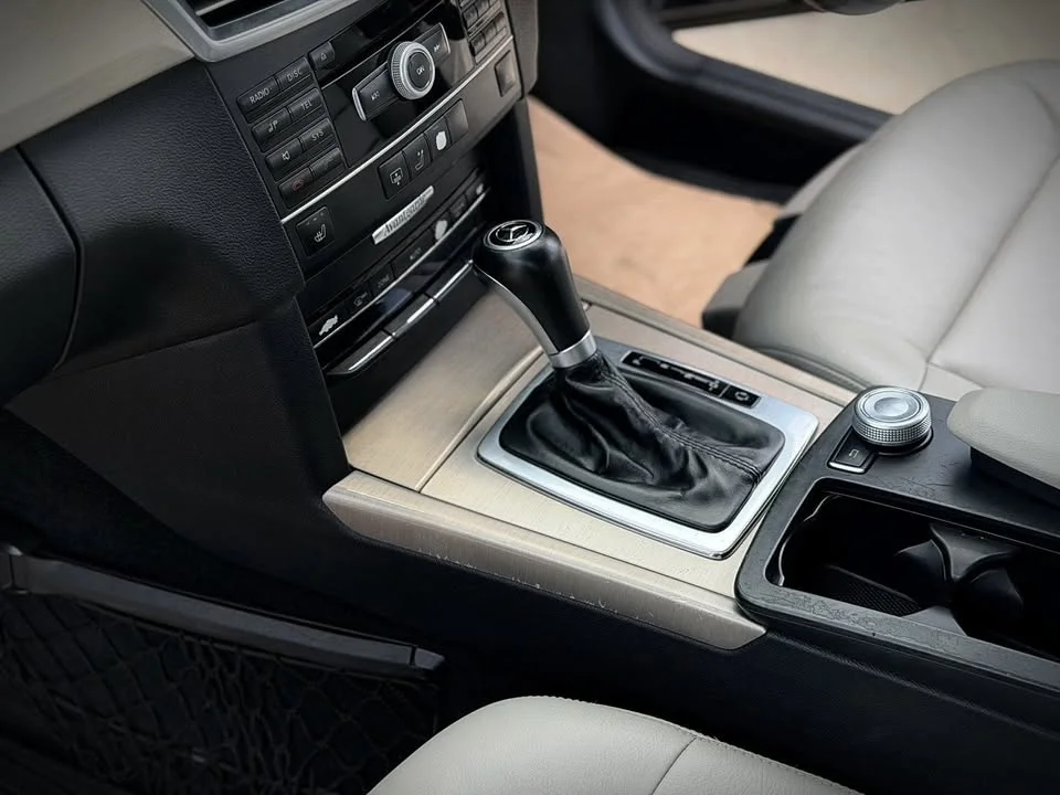 Center console of an older Mercedes E-Class CGI with gear lever, physical switches, rotary controller and brushed trim