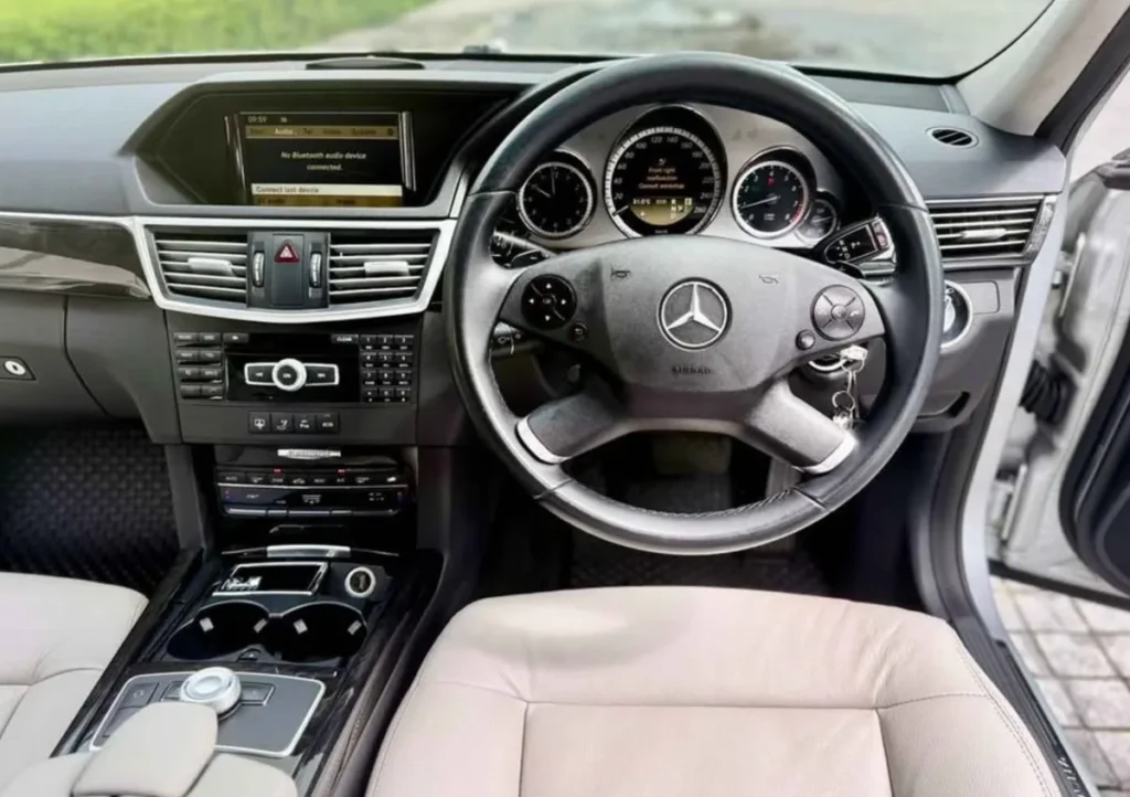 Interior of a Mercedes E250 CDI W212 with analog dials, physical buttons, wood trim and beige leather seats