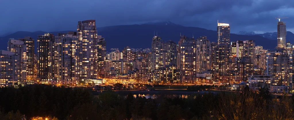 Downtown Vancouver towers lit up at dusk below the North Shore mountains, British Columbia